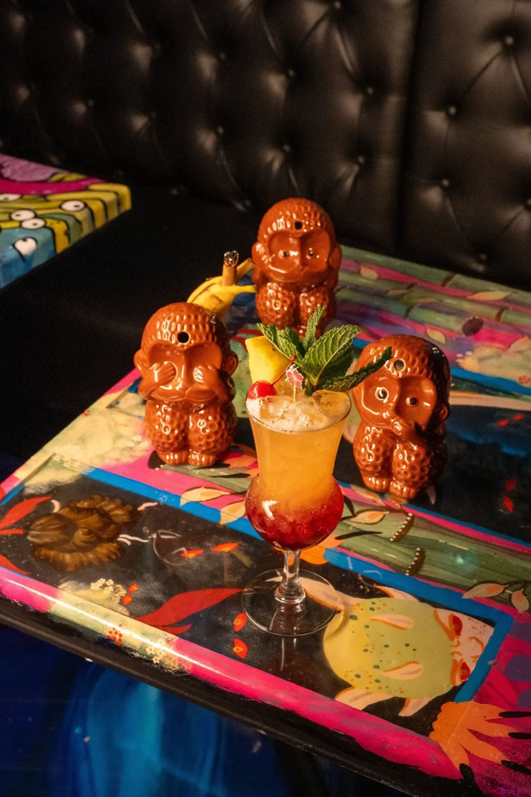 Tiki mugs and a cocktail on a painted table at Endless Bummer