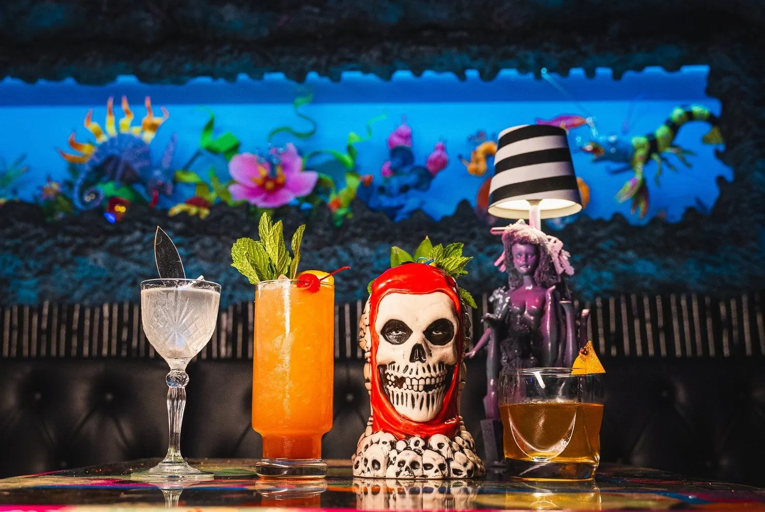 Four Endless Bummer cocktails and the red-hooded skull tiki mug in front of the reef mural